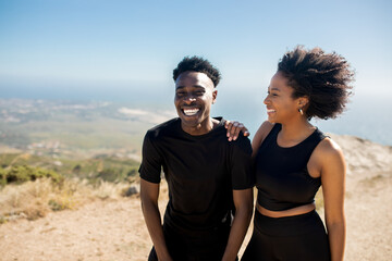 Positive young african american lady and man in sportswear enjoying active lifestyle, training on rocks with ocean view