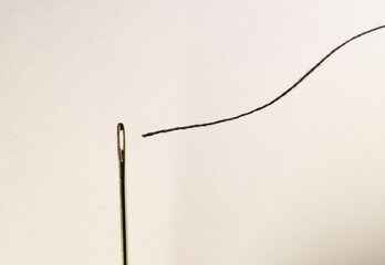 macro view of a sewing needle with black thread about to go into the hole