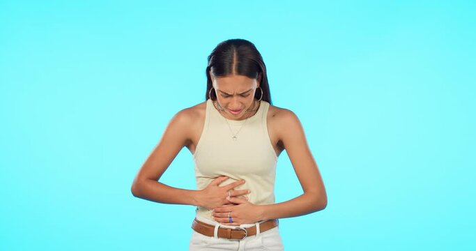 Stomach ache, pms and woman in studio with endometriosis, cramps or menstruation discomfort on blue background. Tummy, anxiety and female person with stress, fibroids or gas, bloated or colon crisis