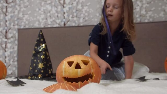 Cute little girl in witch carnival costume having fun with carved halloween pumpkin and holiday attributes. celebrating Halloween with dance
