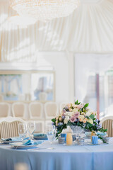 Wedding hall in the restaurant with tables decorated with cloth of blue and pink bouquet of roses and blue delphinium. glasses cutlery candles and candlesticks tablecloth