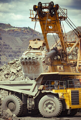 Heavy mining truck and excavator developing the iron ore on the opencast mining site