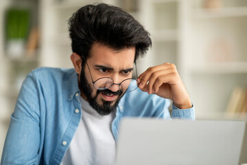Shocked Indian Freelancer Guy Taking Off Glasses And Looking At Laptop Screen