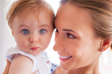 A beautiful young mother embracing her little baby boy with big curious eyes.