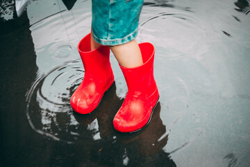 child in red rubber boots holds paper ships in his hands
