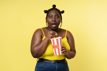 Excited nigerian woman eating popcorn watching movie isolated on yellow background