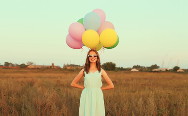 Happy cute smiling young woman with bunch of colorful balloons wearing dress outdoors
