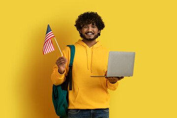 Happy young eastern guy holding laptop and flag of US