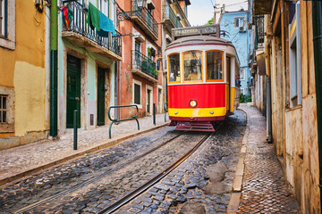 Naklejka na ściany i meble Famous vintage yellow tram 28 in the narrow streets of Alfama district in Lisbon, Portugal - symbol of Lisbon, famous popular travel destination and tourist attraction