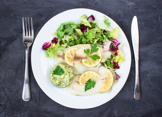 steamed tilapia fish with salad and tartar sauce with appliances on dark background. vertical