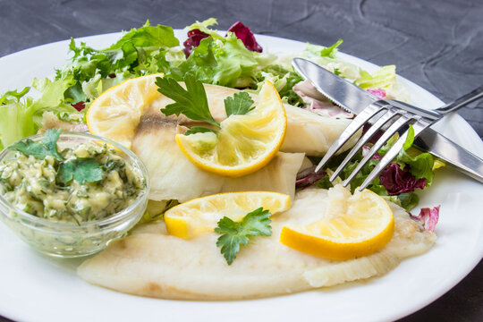 steamed tilapia fish with salad and tartar sauce with appliances on dark background