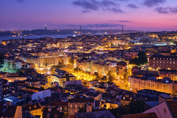Fototapeta na wymiar Night view of Lisbon famous view from Miradouro da Senhora do Monte tourist viewpoint of Alfama and Mauraria old city districts, 25th of April Bridge in the evening twilight. Lisbon, Portugal