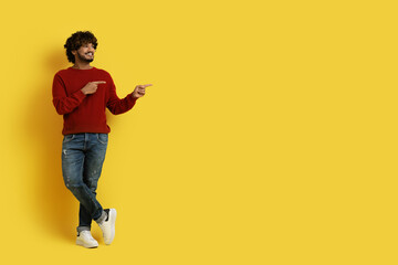 Fototapeta na wymiar Handsome eastern guy pointing at copy space, yellow background