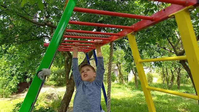 Boy climbing monkey bars on jungle gym outdoors during summer. Strong, happy and wild child is exercising outdoors. Child health, development of physical strength and endurance