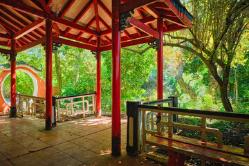 Fototapeta na wymiar Red Chinese style pavilion in lush greenery of asian part of tropical botanical garden in Lisbon, Portugal
