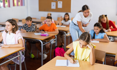 Fototapeta premium Group of school kids with pens and notebooks studying in classroom with teacher