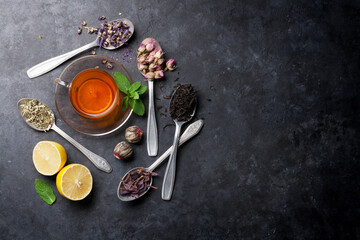 Tea cup and assortment of dry tea in spoons on stone table. Top view with copy space