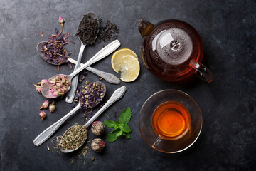 Tea cup, teapot and assortment of dry tea in spoons on stone table. Top view