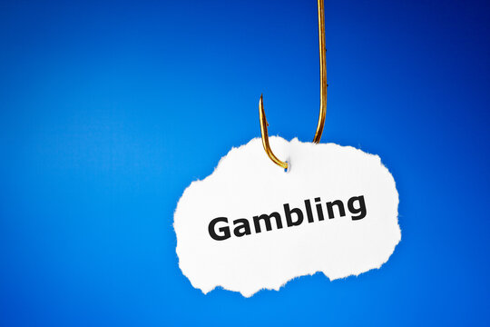 The word Gambling on a piece of paper on fishing hook over blue background. Conceptual image about the risk of addiction to gambling.