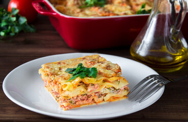 Close-up of a traditional lasagna topped with parskey leafs served on a white plate with fork on dark wooden table