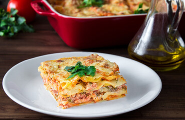 Close-up of a traditional lasagna topped with parskey leafs served on a white plate on dark wooden table