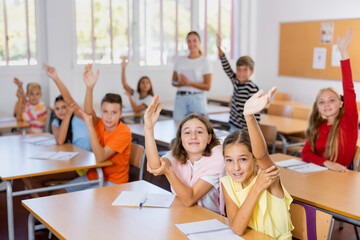 Kids raising hands during lesson in classroom. Clever girls and boys answering teacher's question.