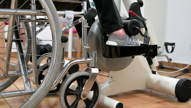 An unrecognizable elderly woman does pedal exercises from wheel chair at hospital. High quality photo.