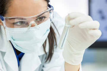 Naklejka premium Female medical or research scientist or doctor using looking at a test tube of clear solution in a lab or laboratory