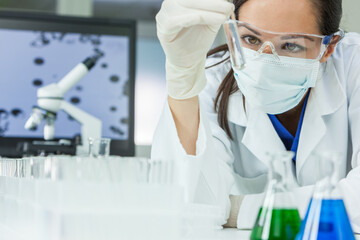 Female medical or research scientist or doctor using looking at a test tube of clear solution in a...