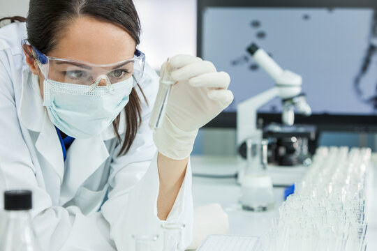 A female medical research scientist or woman doctor looking at a test tube of clear solution in a laboratory with her microscope beside her.