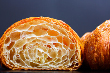 two crunchy delicious croissants at black background, one cut in half