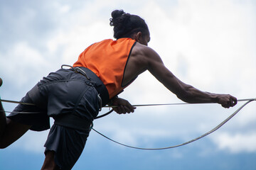 Man using harness hanging on a slackline or tightrope with man bum and orange shirt