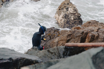 Pescador artesanal vestido de buzo sobre las rocas del mar, pesca artesanal, buceo.