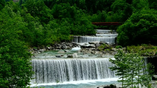 新緑の間を流れる川と砂防堰堤遠くに見える赤い橋
