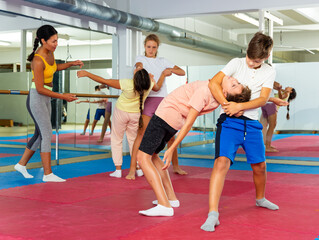 Young children working in pair mastering new self-defense moves at gym during group class