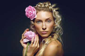 Beautiful blond young woman with pink peony flowers in head and hand. Braided hairstyle. Beauty shot on black background. Copy space. © Designpics