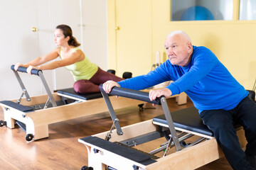 Older man doing exercises of remedial gymnastic on Pilates reformer in rehab clinic. Physical medicine concept ..