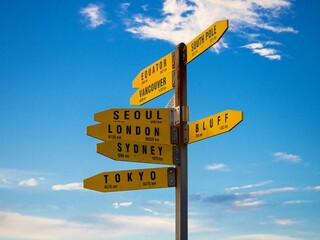 Yellow signpost information pole showing world destinations and direction arrows with blue sky,...