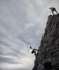 Businessman helps another man to climb a mountain. Businessmen collaborate to achieve a goal...