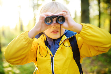 Little boy scout with binoculars during hiking in autumn forest. Child is looking with binoculars.