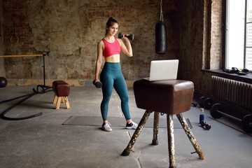 Fototapeta na wymiar Girl trainer leads online fitness class.Young woman doing workout by laptop. Regular sports boosts immune system and promote good health and resistance to diseases.