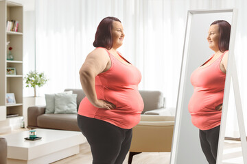 Fototapeta na wymiar Overweight woman in sports clothes standing in front of mirror in a living room