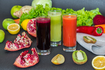 three glasses of different fresh juice. Beet, carrot and kiwi juices on grey background.