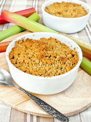 Crumble with rhubarb in two white bowls, stems against a linen tablecloth