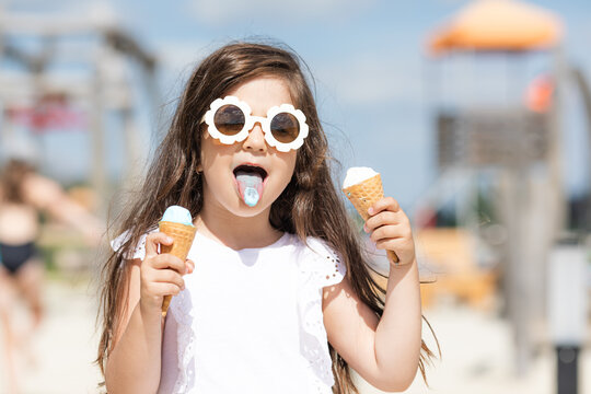 Beautiful little girl in sunglasses and white summer shirt eating an ice cream. High quality photo
