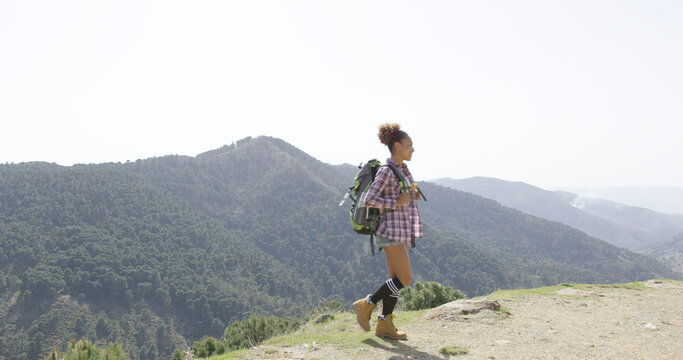 Young fit woman wearing backpack and walking down road on top of mountains with views on background.