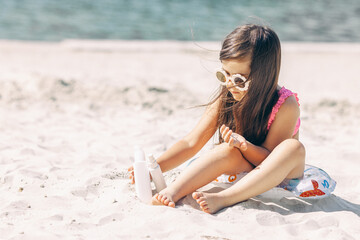 Fototapeta na wymiar Cute little girl using sunscreen cream on a sunny beach. Summer vacation concept
