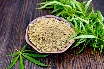 Fototapeta na wymiar Hemp flour in a bowl, cannabis leaves on the background of wooden boards