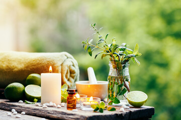 Beautiful spa composition with essential oil, fresh peppermint and burning candles on wooden table outdoors. Selective focus.