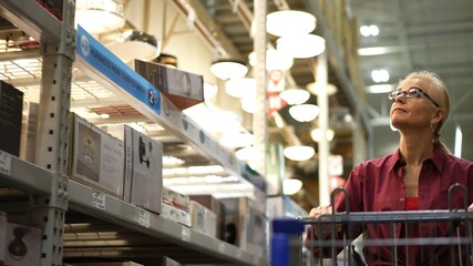 Attractive mature woman pushing shopping cart in lighting section of a large hardware store